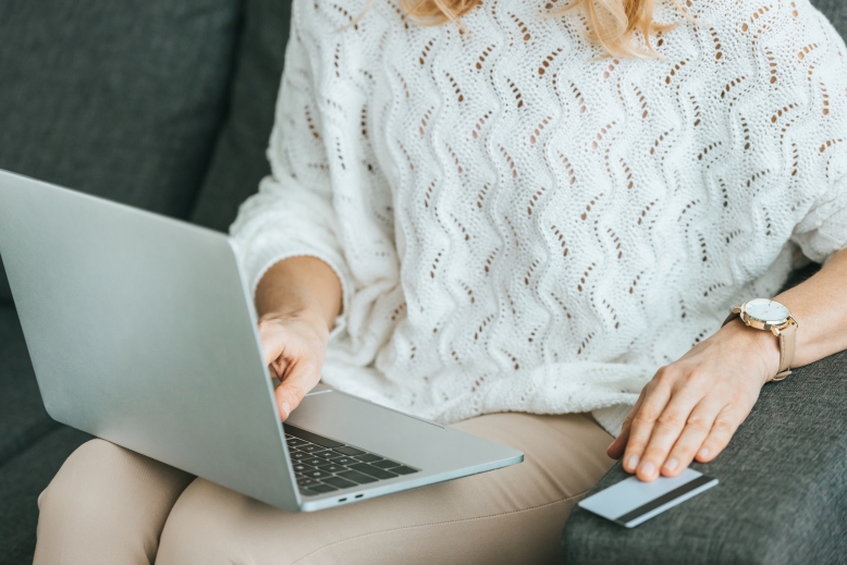 Cropped view of woman using laptop with her credit card on hand.